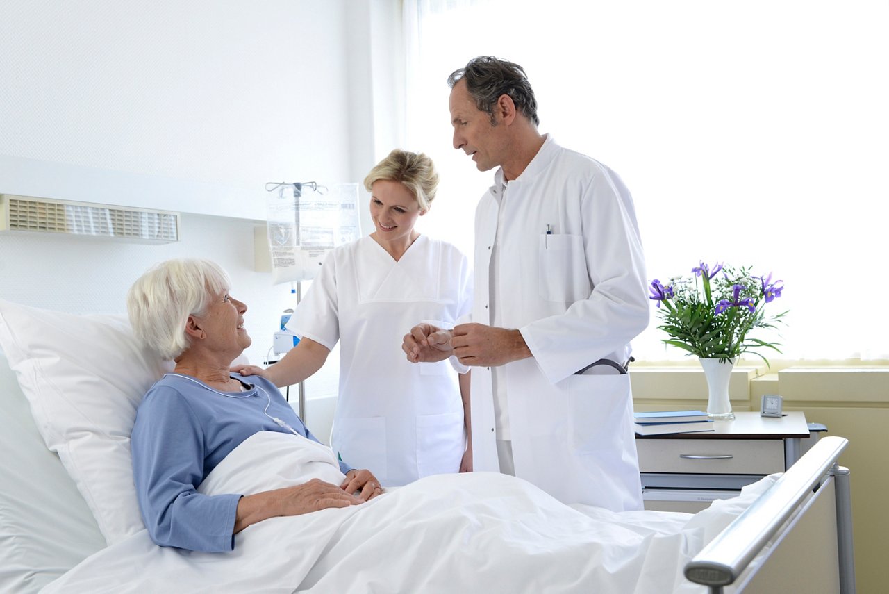 Femme âgée hospitalisée échange souriante avec médecin et infirmière.