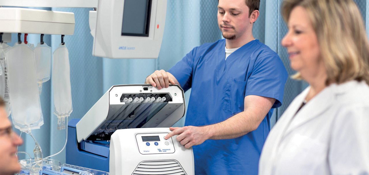 Healthcare professional operating an infusion device beside IV fluid bags in a clinical treatment room.