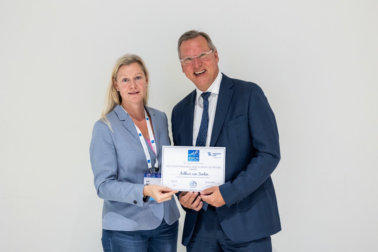 Two people in business attire holding a certificate against a plain background.