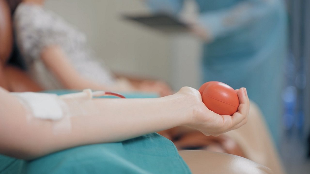 Close-up of a person's arm holding a red stress ball during a blood donation procedure.