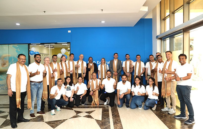 Team photo of Fresenius Kabi India employees in white shirts, smiling and facing the camera in front of a branded blue wall