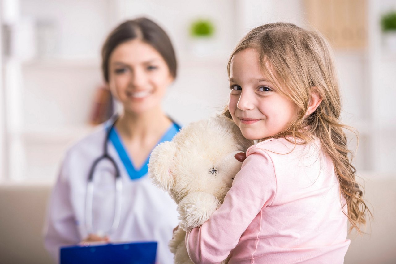 Young smiling female doctor and her little patient  with teddy bear.