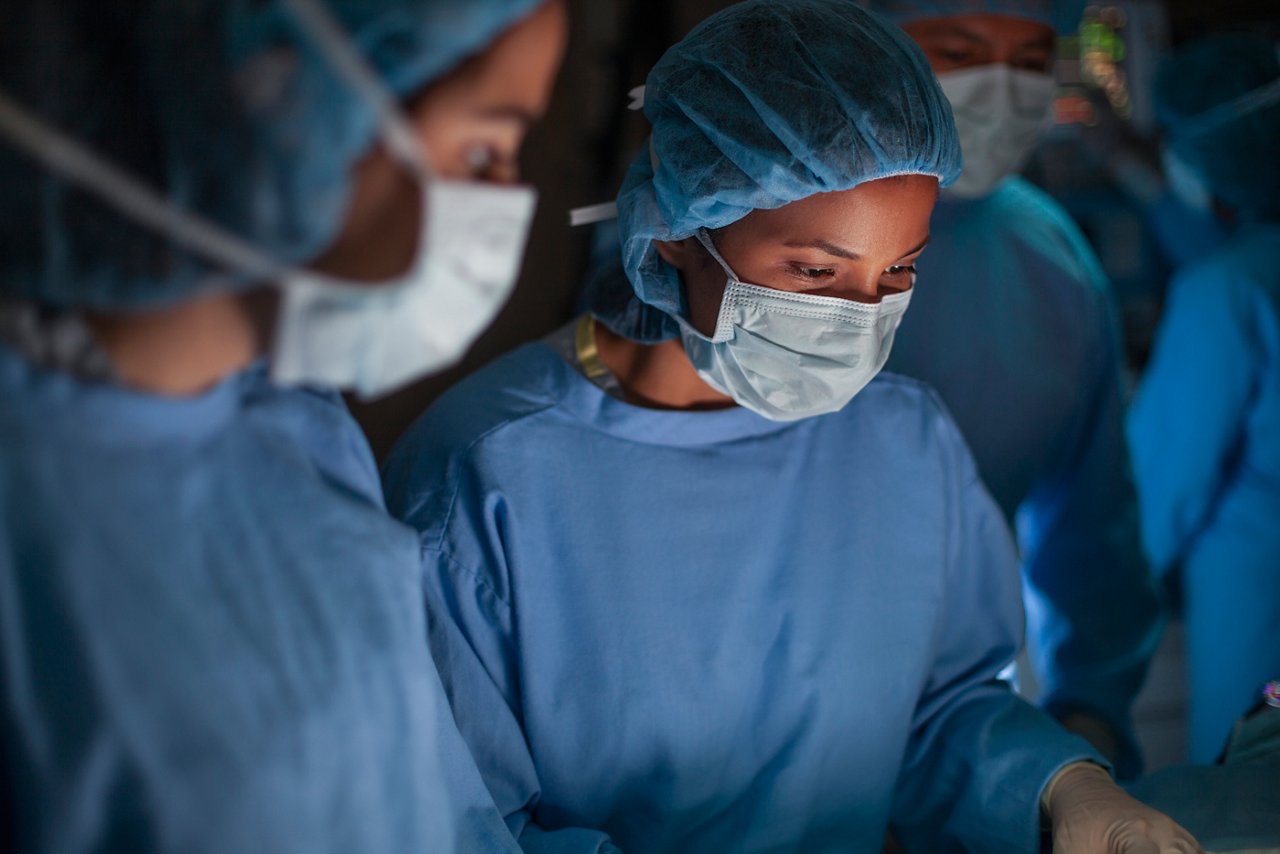 Hispanic medical professional doctor nurse looking down serious in concentration towards patient in surgery operation room in hospital with colleagues