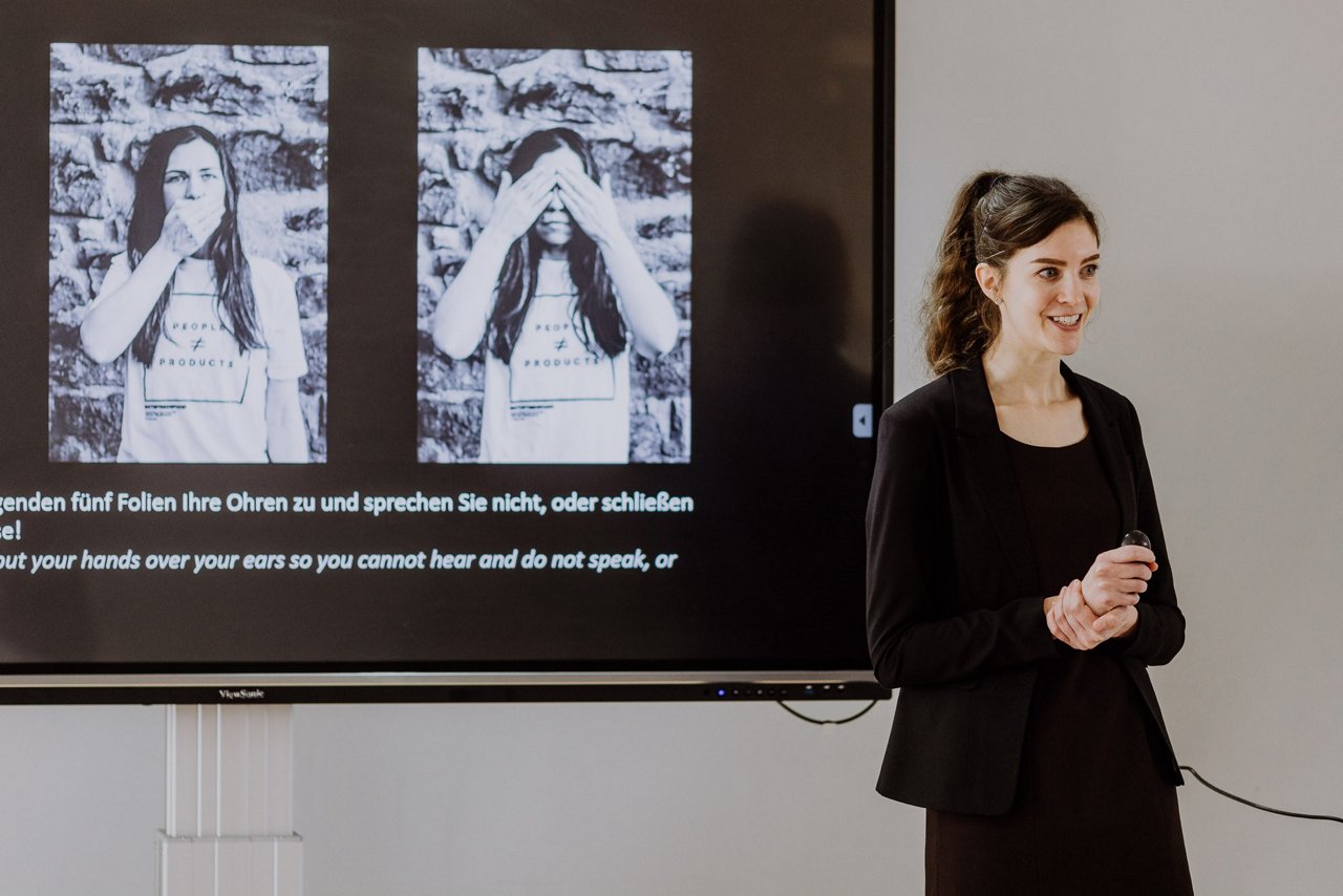 Person stands before a screen showing two images of someone covering their face, with text below.
