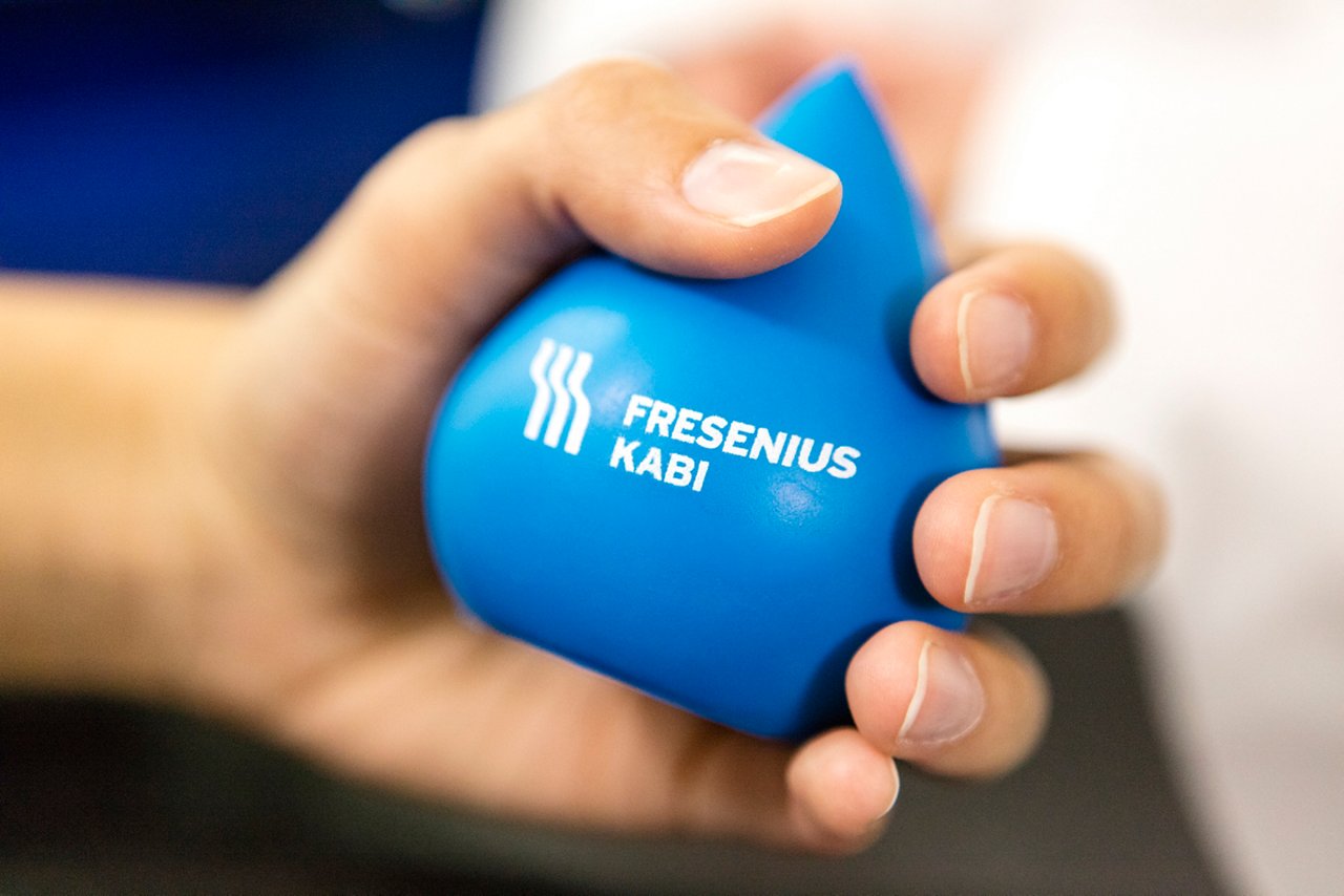hand squeezing a Fresenius Kabi blue stress ball with logo