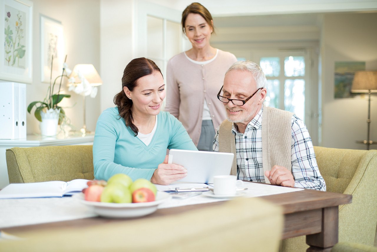 Professionnelle de santé aide un senior à utiliser une tablette, deuxième spécialiste en arrière-plan.