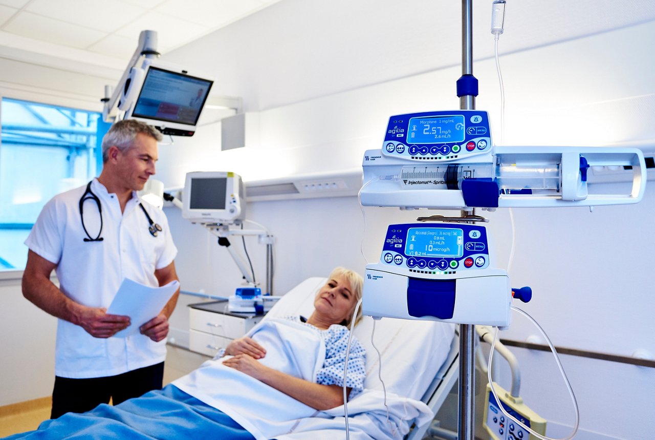 Femme au chevet d'un patient avec une pompe à perfusion, médecin à côté