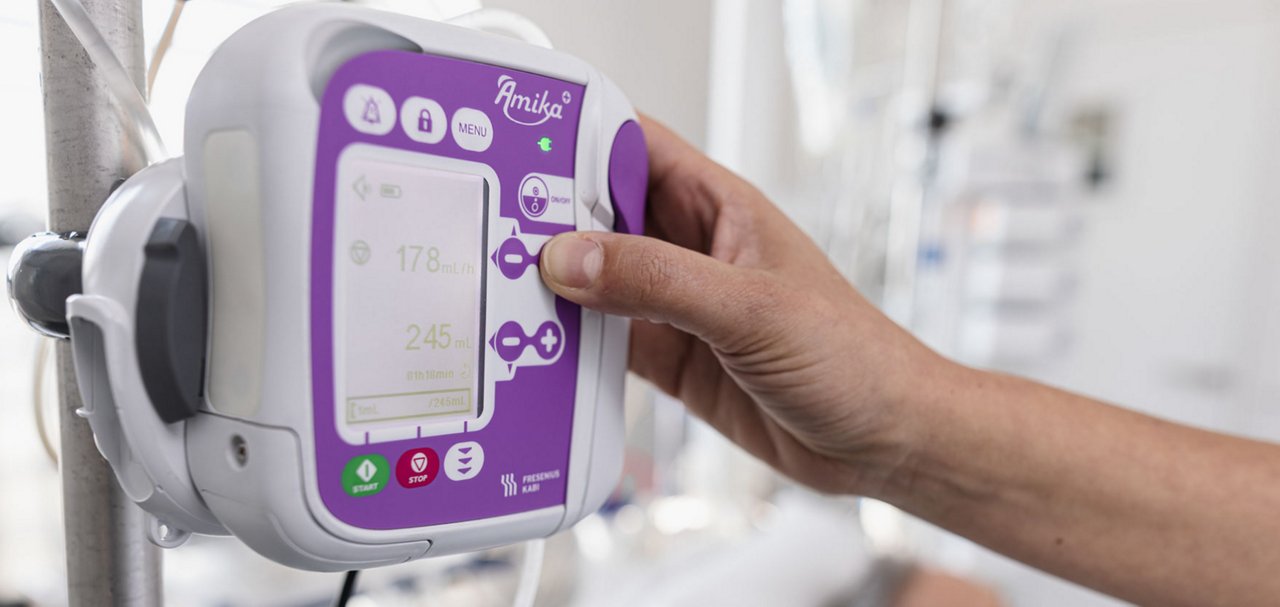 Close-up of a healthcare professional operating an Amika+ infusion pump mounted on an IV pole.