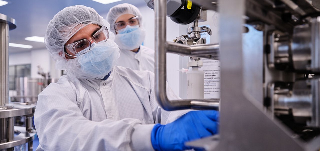 Two people in cleanroom protective clothing working with stainless-steel processing equipment.