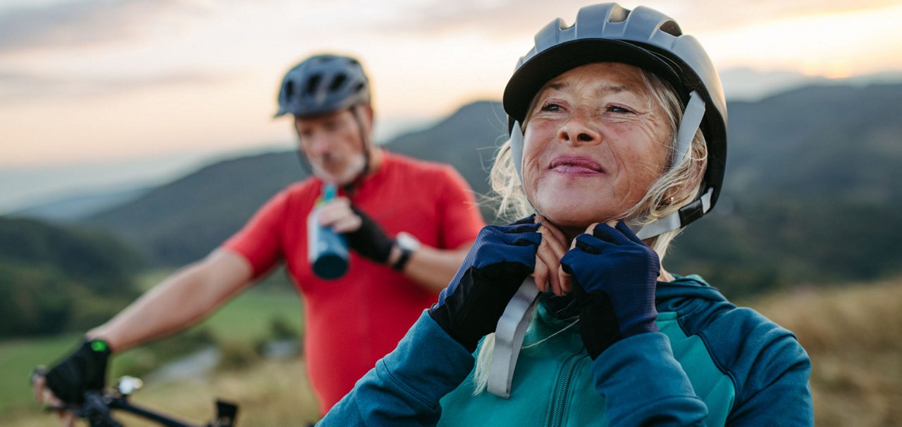 Two cyclists pause outdoors while one adjusts a helmet before continuing a ride.