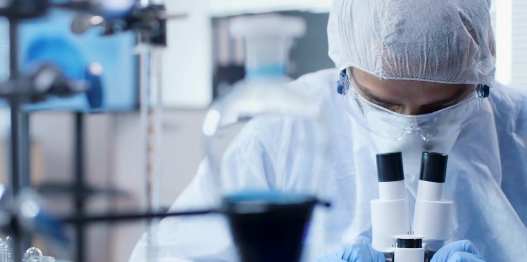 A scientist in protective gear working with a microscope.