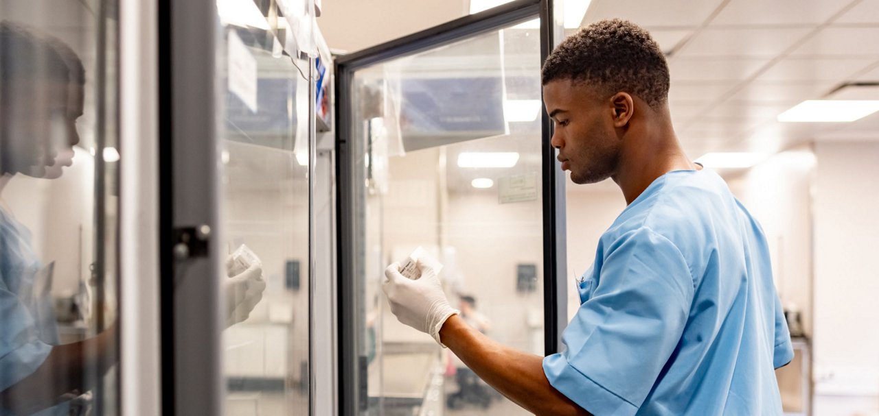 Healthcare professional examining medical products in a refrigerated storage unit.