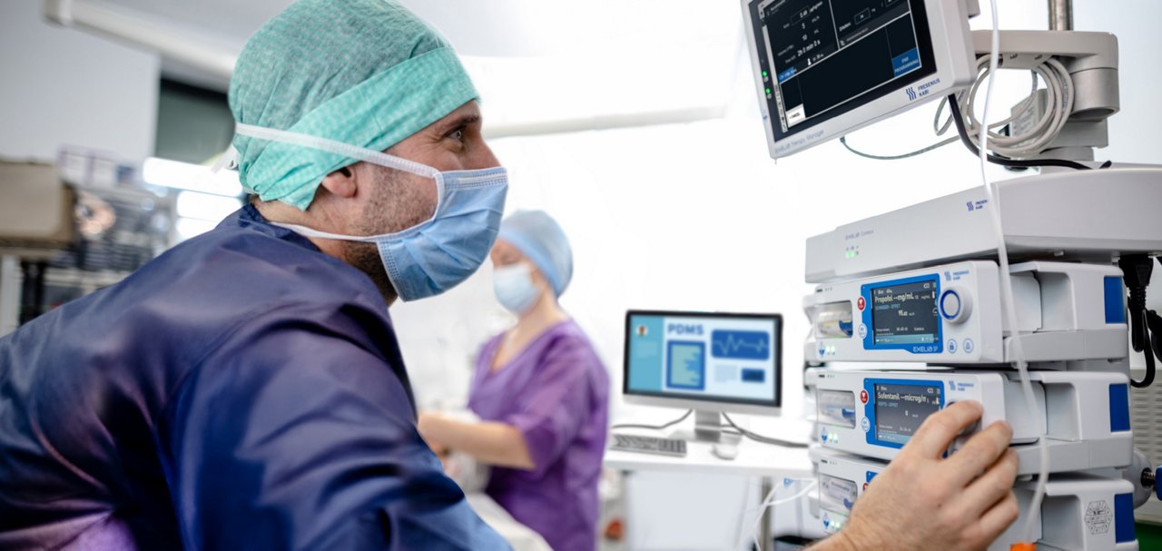 Healthcare professional adjusting an infusion workstation with multiple infusion pumps and monitoring equipment in a clinical setting.