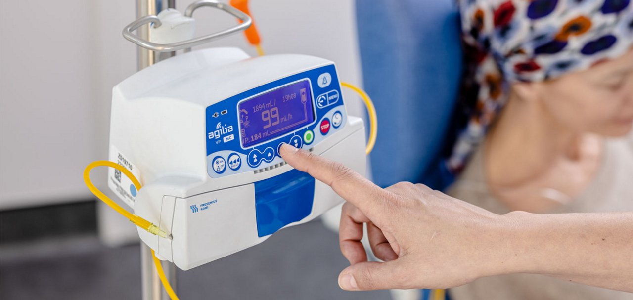 Hand pressing controls on an electronic infusion pump attached to an IV pole.