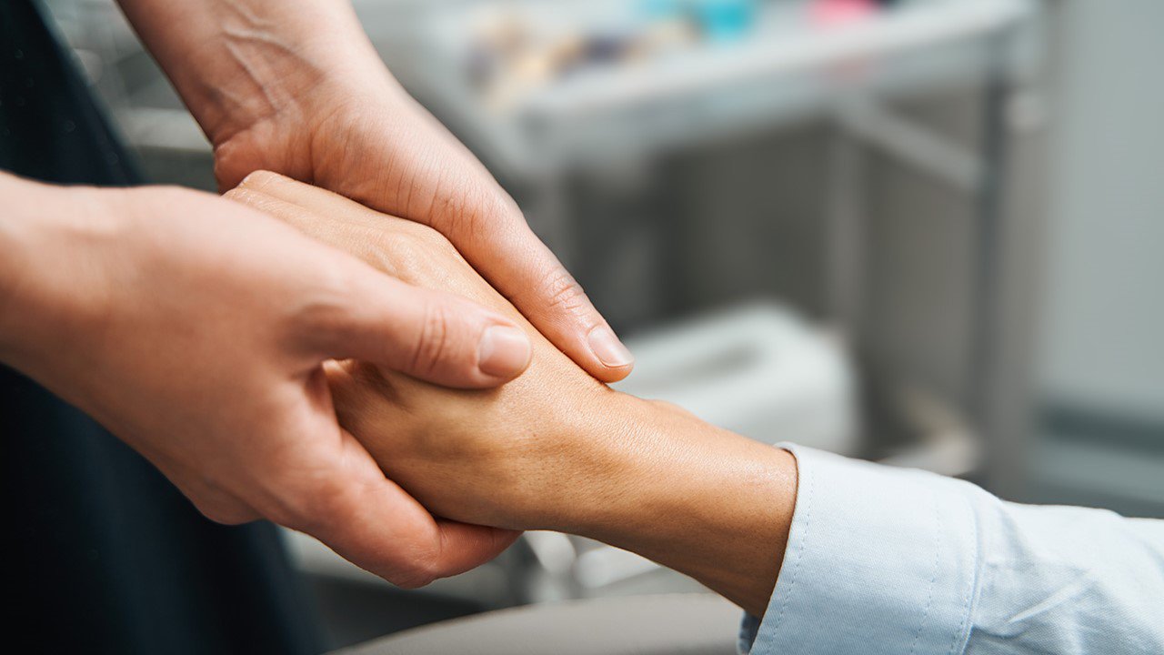 The image features a close-up of two hands gently holding each other, symbolizing support and unity.