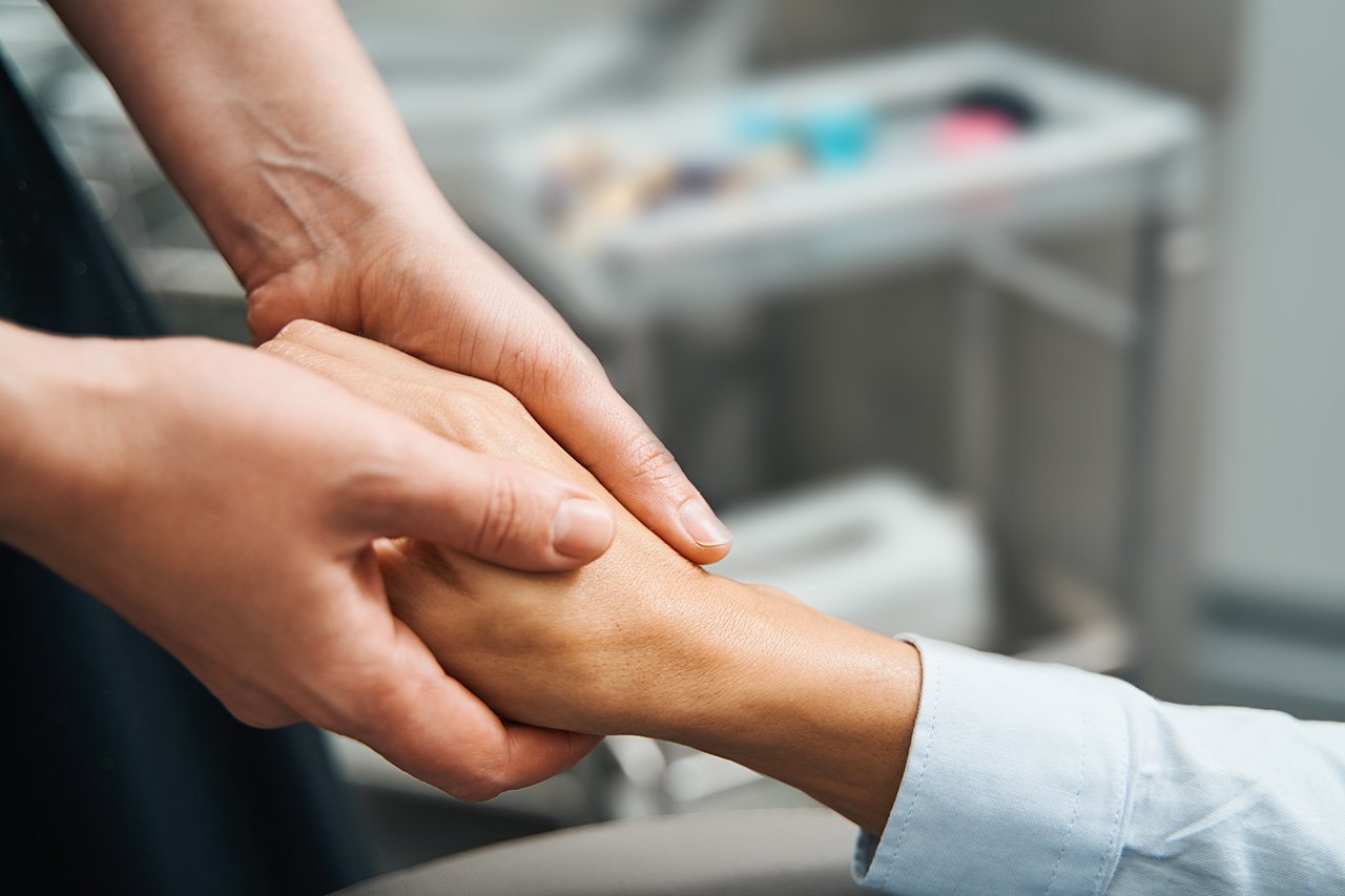 The image features a close-up of two hands gently holding each other, symbolizing support and unity.