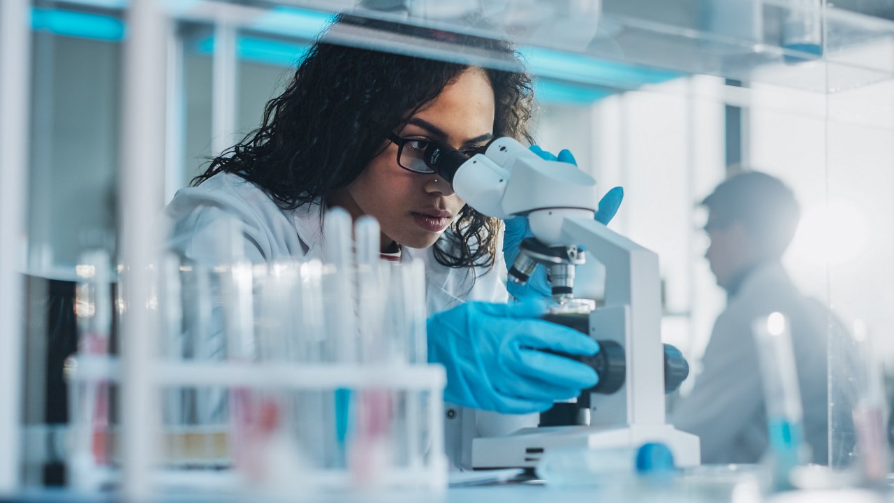 Medical Science Laboratory: Portrait of Beautiful Black Scientist Looking Under Microscope Does Analysis of Test Sample. Ambitious Young Biotechnology Specialist, working with Advanced Equipment