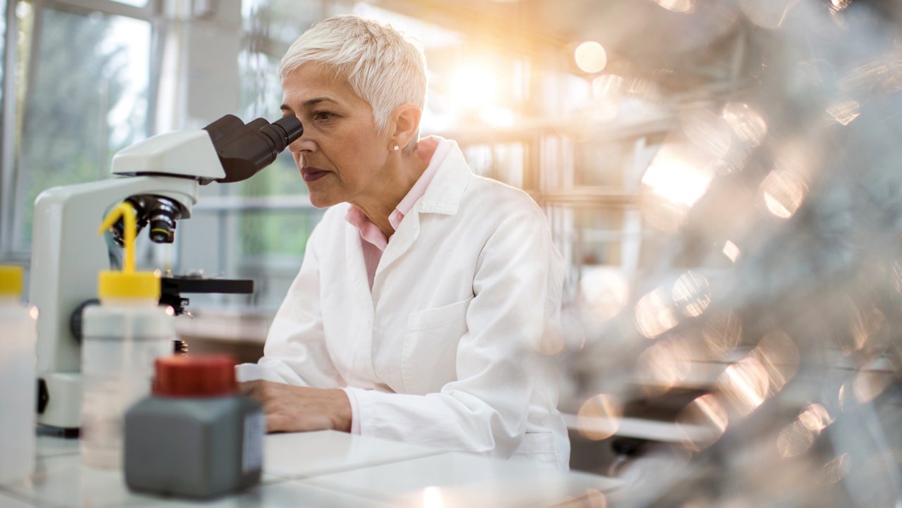 Mature scientist looking through a microscope in a laboratory.