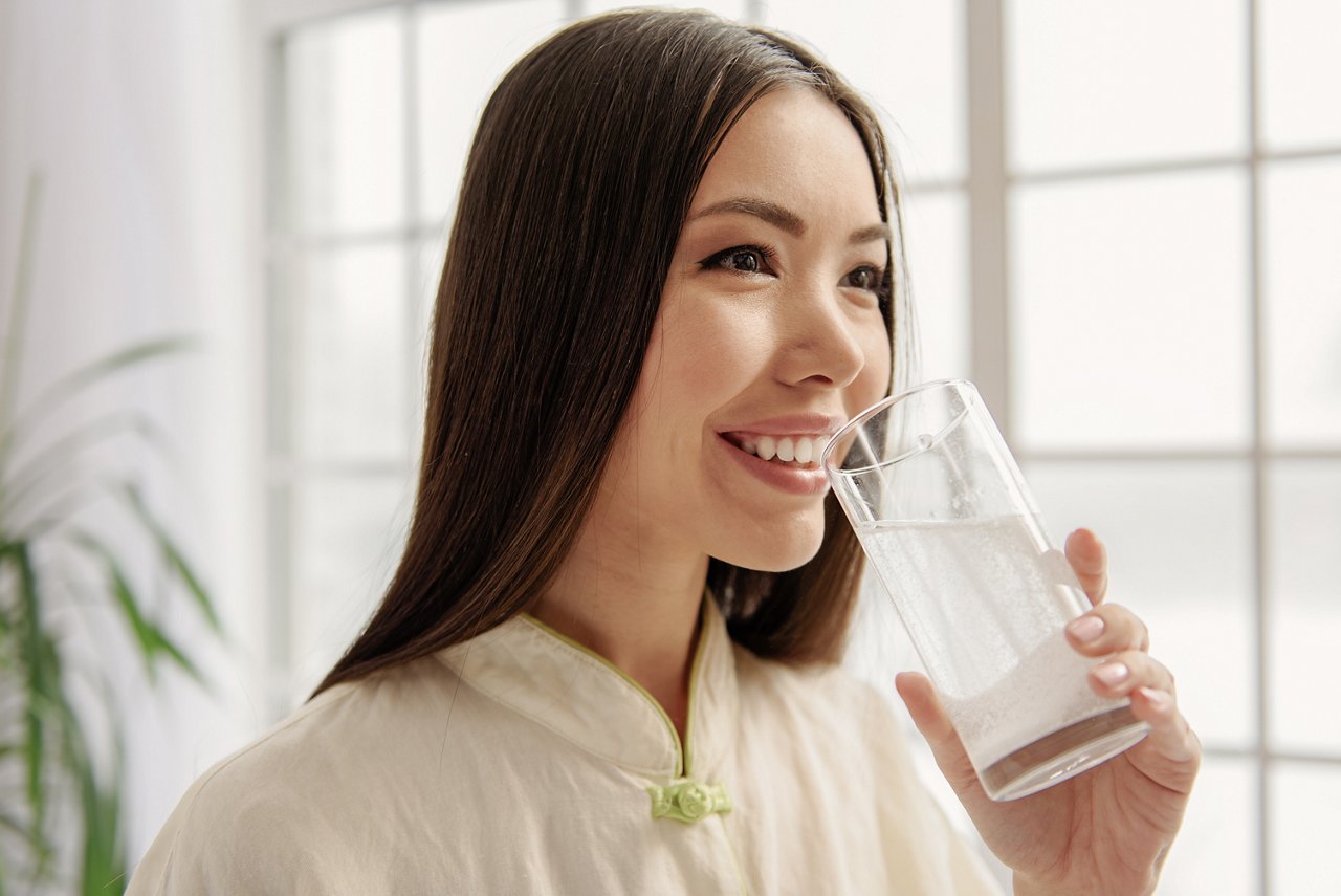 Cheerful asian woman taking liquid with medicament while looking away. Health concept