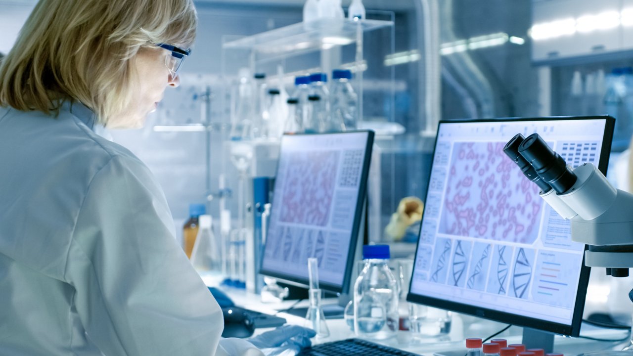 Senior Female Scientist Works with High Tech Equipment in a Modern Laboratory. Her Colleagues are Working Beside Her.