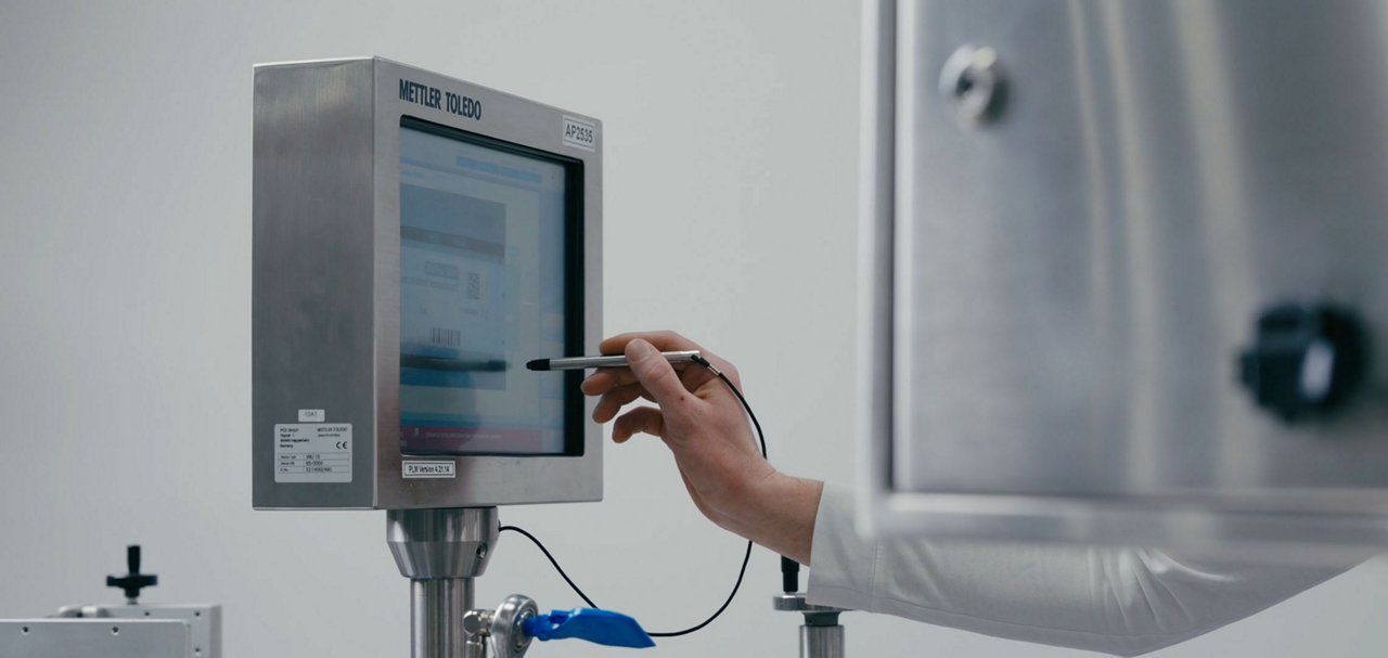 Person using a stylus to operate a touchscreen on stainless-steel processing equipment.