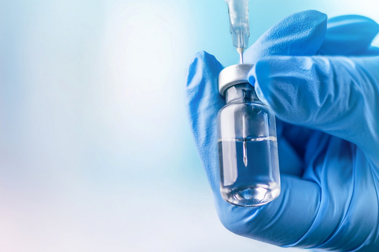 Doctor's hand holding glass vial and syringe with injection over blue background. Vaccination or beauty therapy concept.