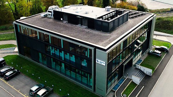 Aerial view of a modern rectangular office building with glass windows and cars parked around it.