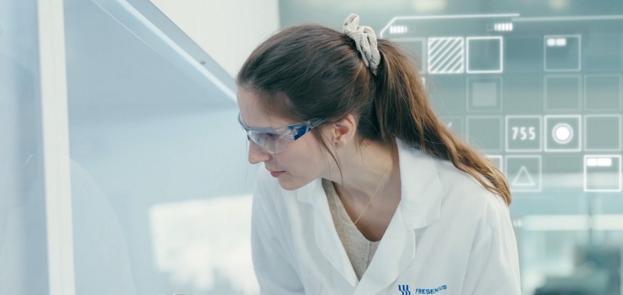 Person wearing protective eyewear and a lab coat working beside laboratory equipment and a digital interface.