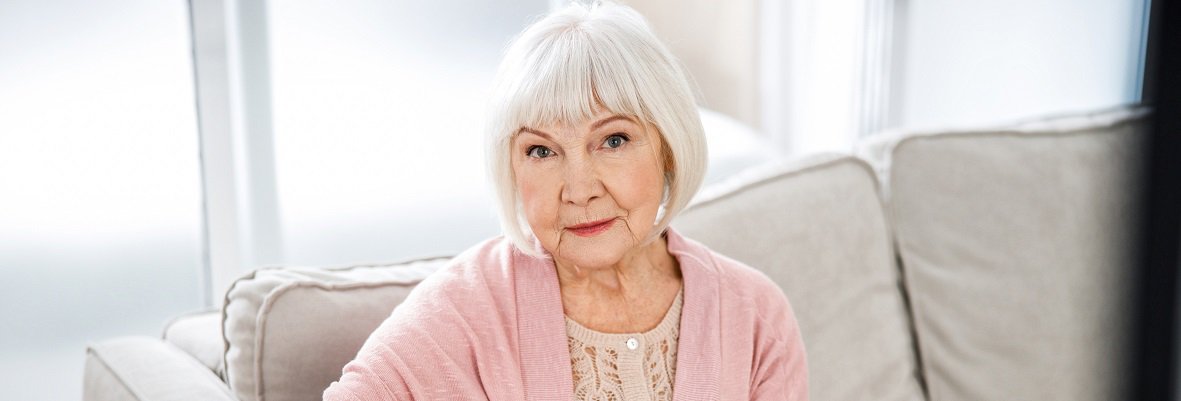 ältere Dame sitzt auf der Couch und schaut in die Kamera