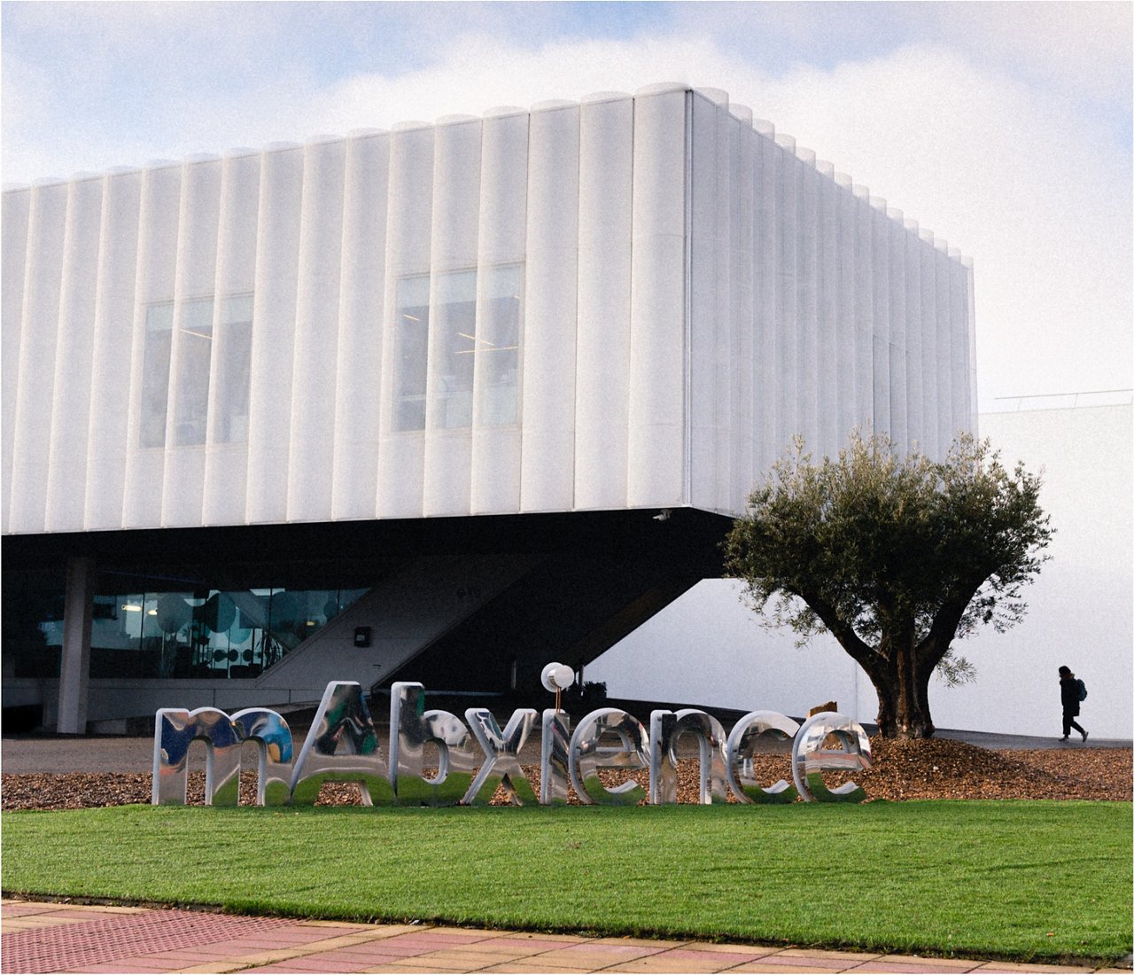 Modern white office building with a metallic mAbxience sign on a landscaped lawn in front of the entrance.