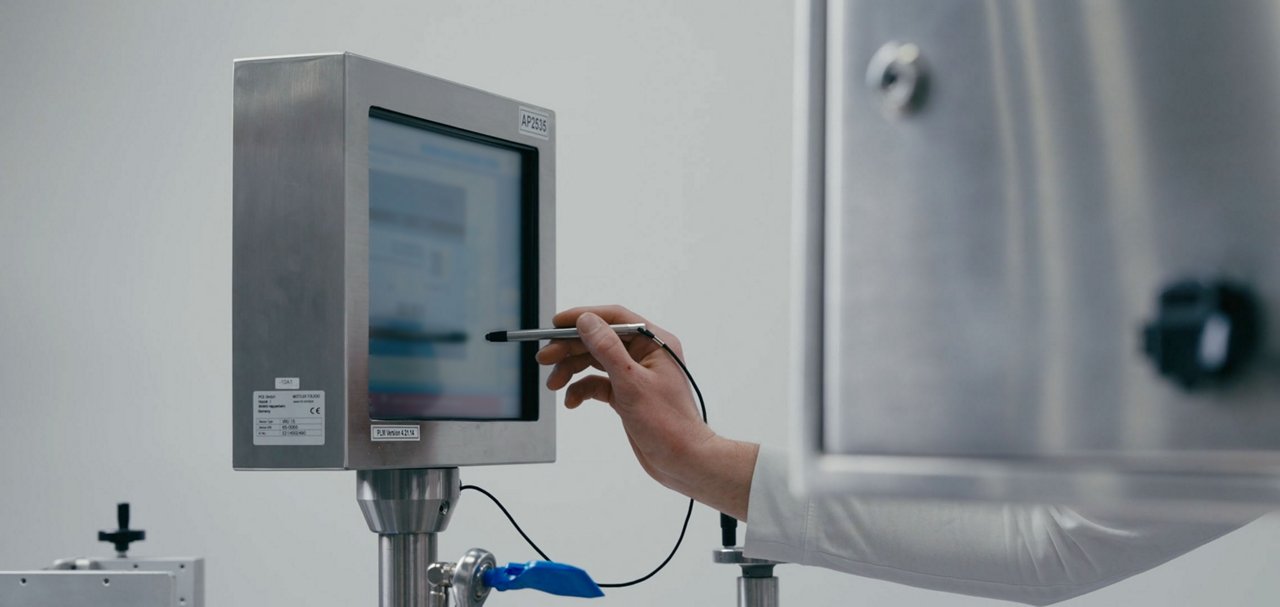 Hand operating a touchscreen control panel beside industrial production equipment