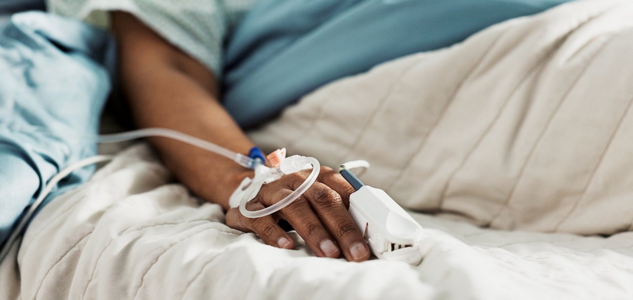 Patient hand with intravenous line and monitoring clip while resting in a hospital bed.