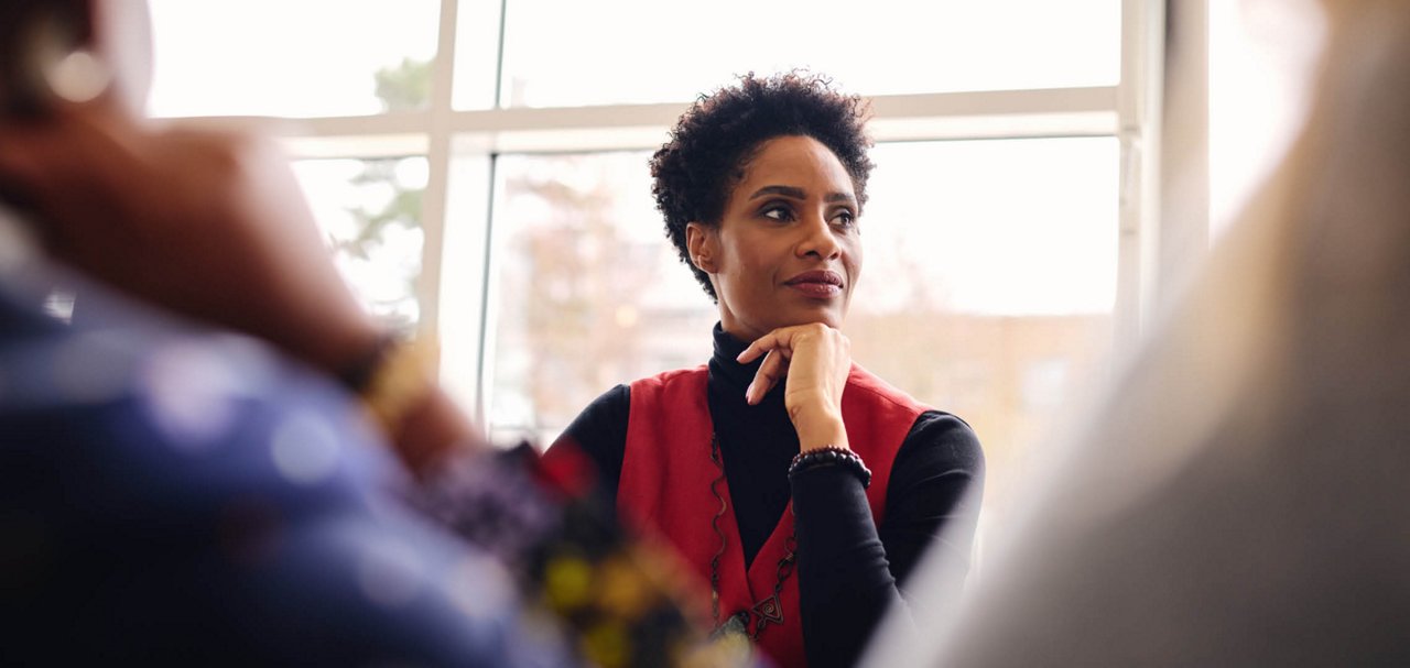 Person seated by large windows participating in a conversation with others.