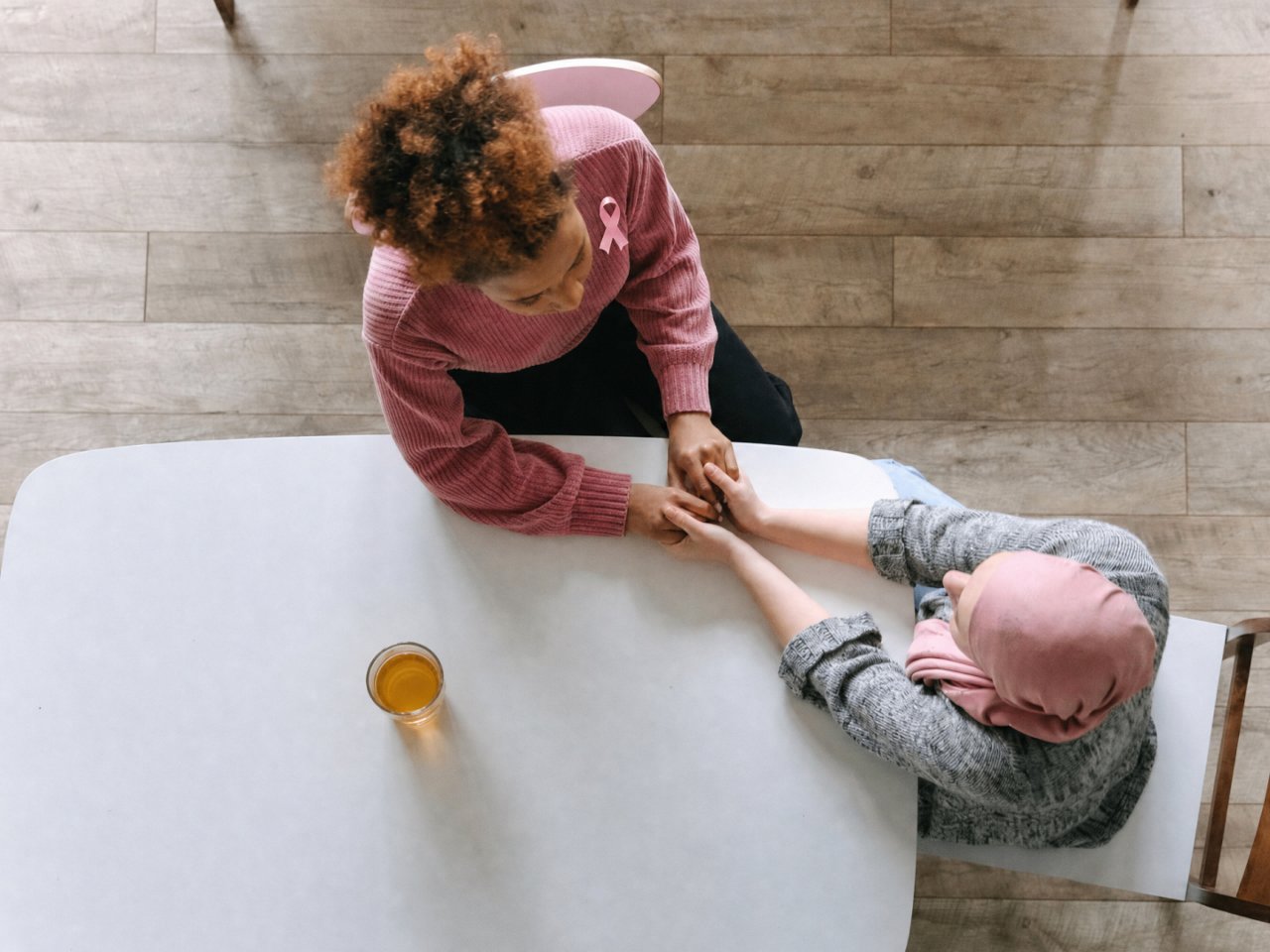Two people holding hands across a table, with one wearing a pink breast cancer awareness ribbon.