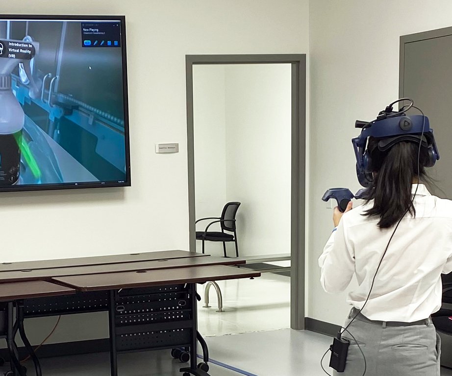 A woman engages in cleanroom training using virtual reality equipment, interacting with a simulated environment on-screen.